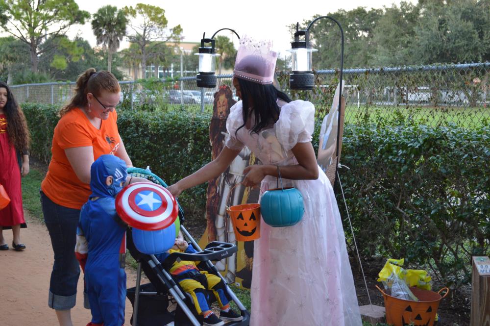 Young woman dressed in pink dress hands candy to boy dressed in Captain America costume